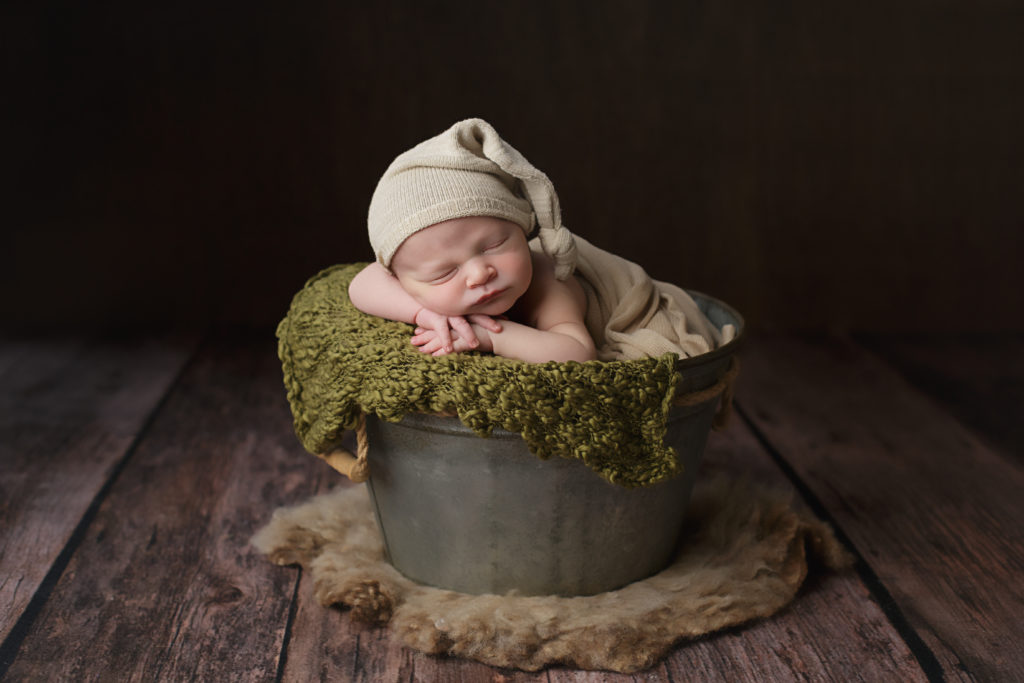 Baby boy posed in a pail and wearing a cute little hat.